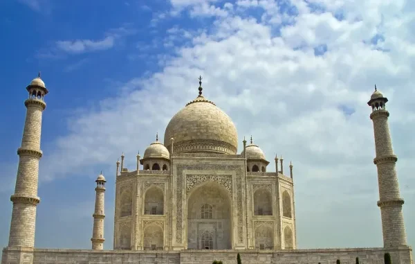The white marble Taj Mahal in Agra, India, framed by a blue sky with soft white clouds, representing bespoke luxury travel.