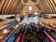 A group of people lying down on yoga mats during a sound healing meditation session in a wooden A-frame barn attic, with Tibetan singing bowls arranged on a colorful blanket in the foreground.