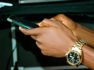 Close-up of a person's hands holding a smartphone, wearing a gold watch, representing mobile sports betting and placing accumulator bets in Zambia.