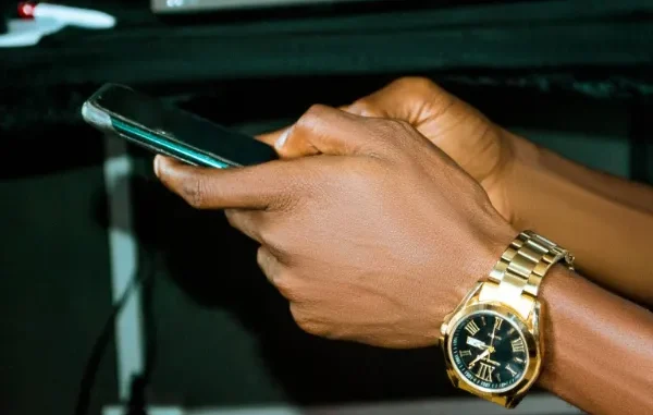 Close-up of a person's hands holding a smartphone, wearing a gold watch, representing mobile sports betting and placing accumulator bets in Zambia.
