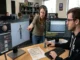 A game engineer and art director leaning over a dual-monitor workstation inspecting a 3D character asset in a game engine to resolve pivot point and naming convention issues.