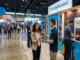 A booth representative handing a sleek matte black reusable water bottle to an attendee at a trade show event.