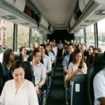 A diverse group of passengers smiling and socializing inside a spacious, modern charter bus driving past Brooklyn brownstones.