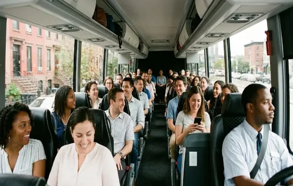 A diverse group of passengers smiling and socializing inside a spacious, modern charter bus driving past Brooklyn brownstones.
