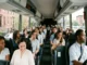 A diverse group of passengers smiling and socializing inside a spacious, modern charter bus driving past Brooklyn brownstones.
