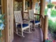 Two wooden teak rocking chairs with blue cushions placed on a rustic cabin porch with a small side table.