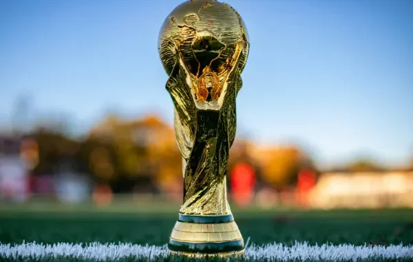 Close-up of the official golden FIFA World Cup trophy standing on the white touchline of a green soccer pitch.