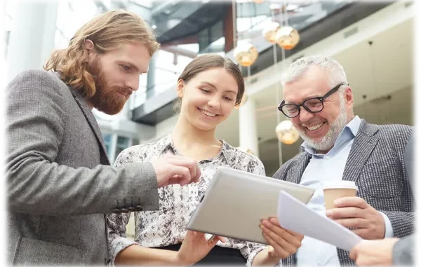 An HR consultant reviewing strategy documents on a tablet with two diverse colleagues in a modern office building.