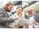 An HR consultant reviewing strategy documents on a tablet with two diverse colleagues in a modern office building.