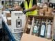 A man in a yellow vest in a warehouse is standing next to two open boxes. One box is for a single bottle and the other is for four bottles. Both boxes are packed with protective materials to prevent damage during shipping.
