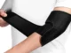 Person wrapping a black adjustable neoprene elbow brace with a Velcro strap around their arm for joint support.