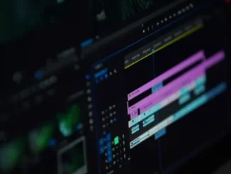 A close-up photograph of a computer screen displaying a complex video editing software timeline with multiple colored video and audio tracks, playback controls, and keyframe markers in a dark-mode interface.