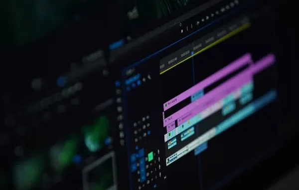 A close-up photograph of a computer screen displaying a complex video editing software timeline with multiple colored video and audio tracks, playback controls, and keyframe markers in a dark-mode interface.