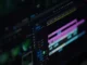 A close-up photograph of a computer screen displaying a complex video editing software timeline with multiple colored video and audio tracks, playback controls, and keyframe markers in a dark-mode interface.