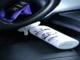 A white car interior cleaner spray bottle placed on a black leather seat next to a steering wheel and purple microfiber cloth.