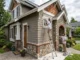 Professional painters carefully applying paint to white window trim and inspecting stone masonry on a modern mixed-material home with cedar shake and lap siding.