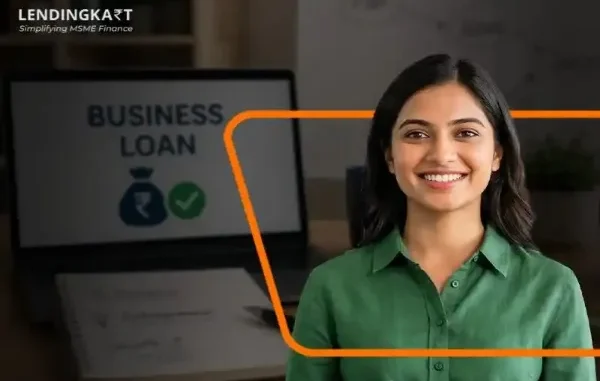 Smiling Indian female entrepreneur standing in front of a laptop displaying a business loan approval graphic.