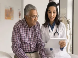 A smiling female doctor holding a tablet while explaining health insurance coverage options to an elderly man sitting in a clinic.