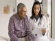 A smiling female doctor holding a tablet while explaining health insurance coverage options to an elderly man sitting in a clinic.