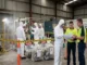 Industrial facility manager and contractor reviewing building schematics outside a safety-barricaded asbestos containment zone in a warehouse.