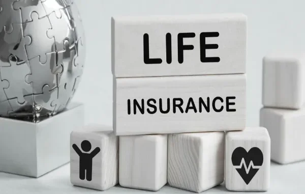 Wooden blocks spelling out "LIFE INSURANCE" above smaller blocks featuring icons of a person and a heart with a pulse line, placed beside a metallic puzzle globe.