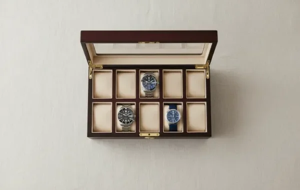 An open wooden watch display box with ten slots, containing only three wristwatches, symbolizing a growing collection.