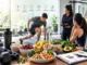 A selection of healthy foods, including berries, oats, eggs, and a meal bowl, arranged on a table in front of people training and consulting in a gym setting.
