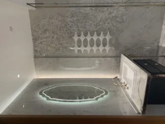 Modern white geometric towel warmer mounted on a grey marble wall above an illuminated bathroom vanity.