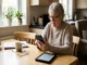 Elderly woman with furrowed brow looking confused at a smartphone screen, with a tablet nearby, highlighting usability struggles.