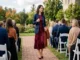 A woman in a burgundy dress and navy blazer walking at an outdoor September wedding.