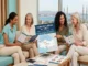 A group of international patients reviewing brochures and consulting a poster titled "Cosmetic Surgery in Turkey: International Patients Guide" in a modern medical office overlooking the Istanbul skyline.