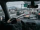 View from inside a car driving on a snowy I-25 highway toward the Denver skyline and mountains in winter.