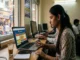 A candid photograph of a woman focusing on a laptop screen displaying the "66 Lottery" platform. She is in a Delhi cyber cafe with other people working nearby.