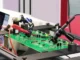 Green printed circuit board undergoing automated probe testing during rapid turnkey PCB assembly service.