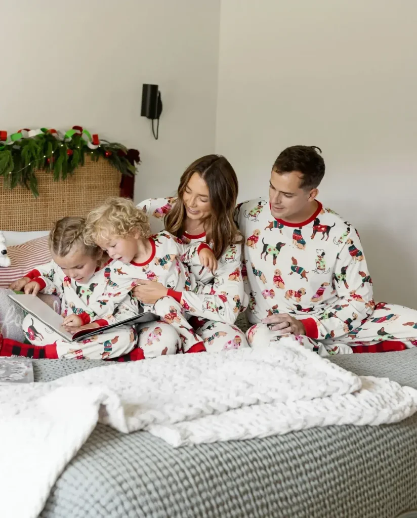 Family sitting together on a bed in matching dog-pattern holiday pajamas while reading a book.