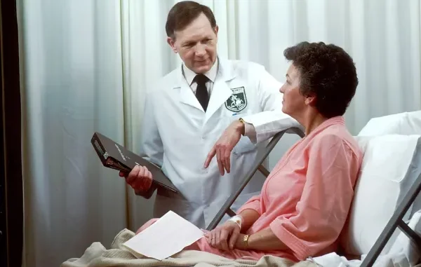 A doctor in a white lab coat discussing medical records with a patient resting in a hospital bed.