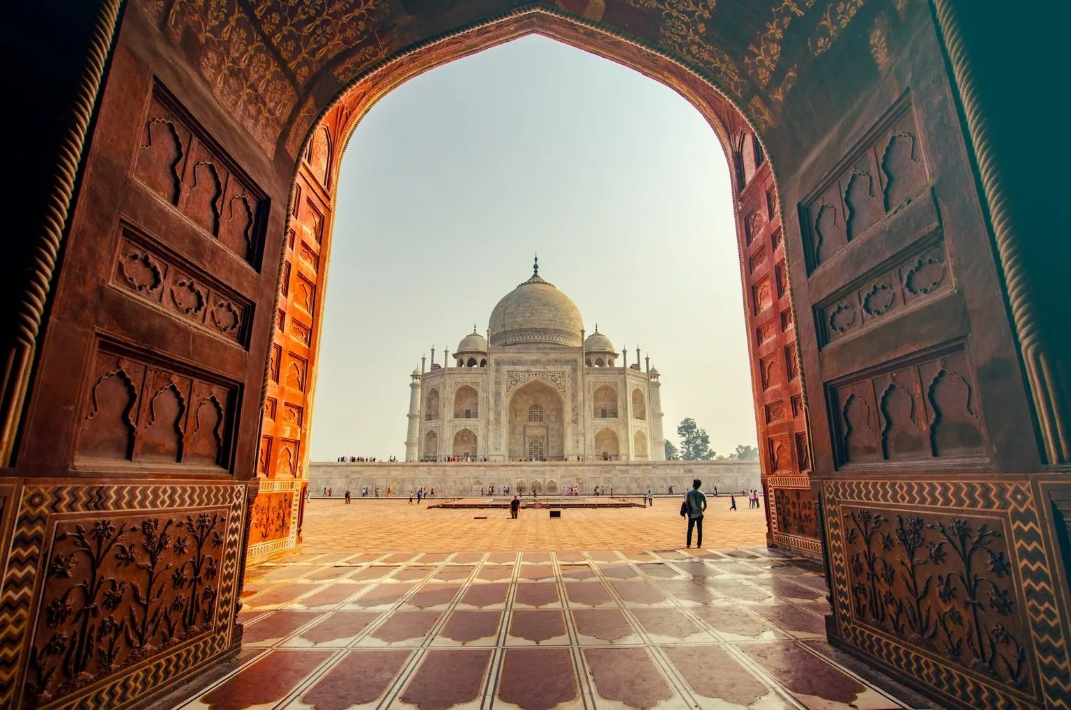 View of the Taj Mahal in Agra, India, framed through an ornate red sandstone archway, representing departure and relocation to Portugal.