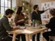 A professional team collaborating in a modern office meeting, taking notes on digital tablets and stylus devices around a wooden table.