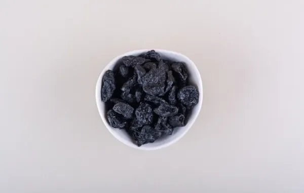A white bowl filled with dark, resinous Shilajit pieces set against a neutral background, highlighting its traditional use in wellness practices.