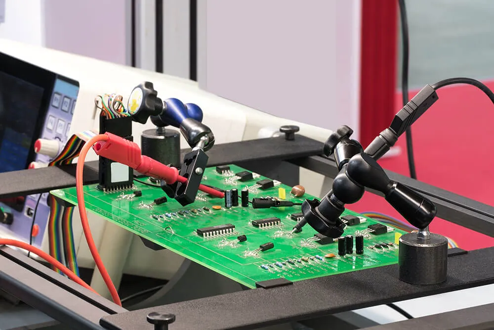 Close-up of a green PCB prototype undergoing functional circuit testing with precision probe clamps on a workbench.
