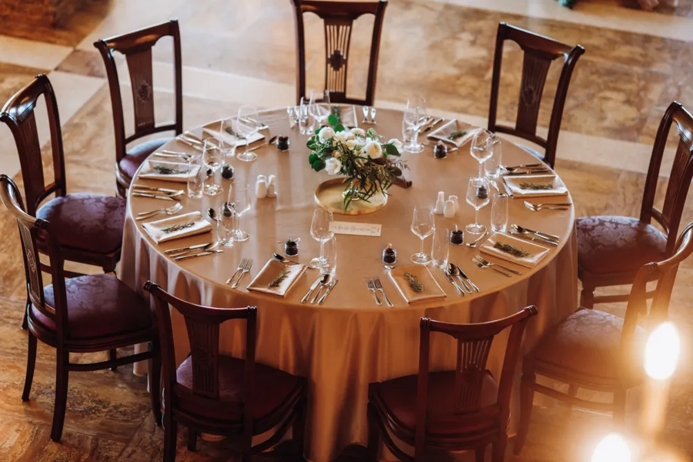 Overhead view of a round banquet table set with rented gold-toned place settings, matching napkins, glassware, and cutlery for a wedding reception.