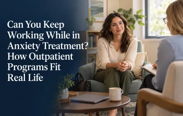 A smiling woman sitting comfortably in an armchair during an outpatient therapy session, speaking with a therapist taking notes in a bright, cozy office setting.